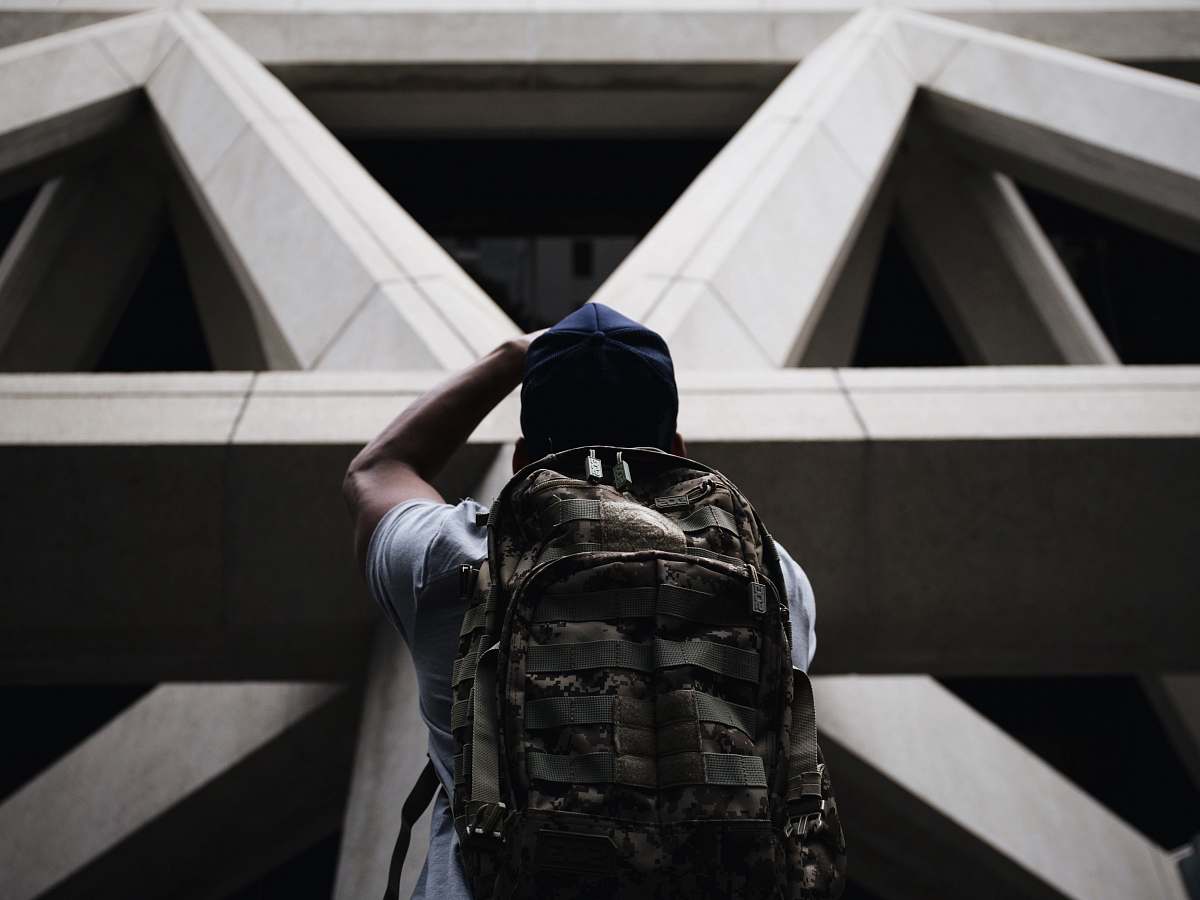 san francisco person wearing shirt and hiking bag looking in front of grey concrete structure while standing during daytime triangle